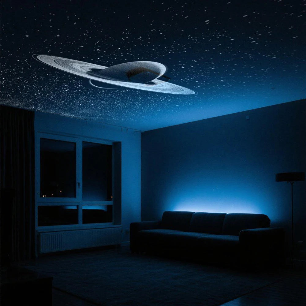 Salón oscuro con sofá iluminado en tonos azules por el proyector espacial Lovuris Nova mostrando el planeta Saturno y estrellas en el techo.